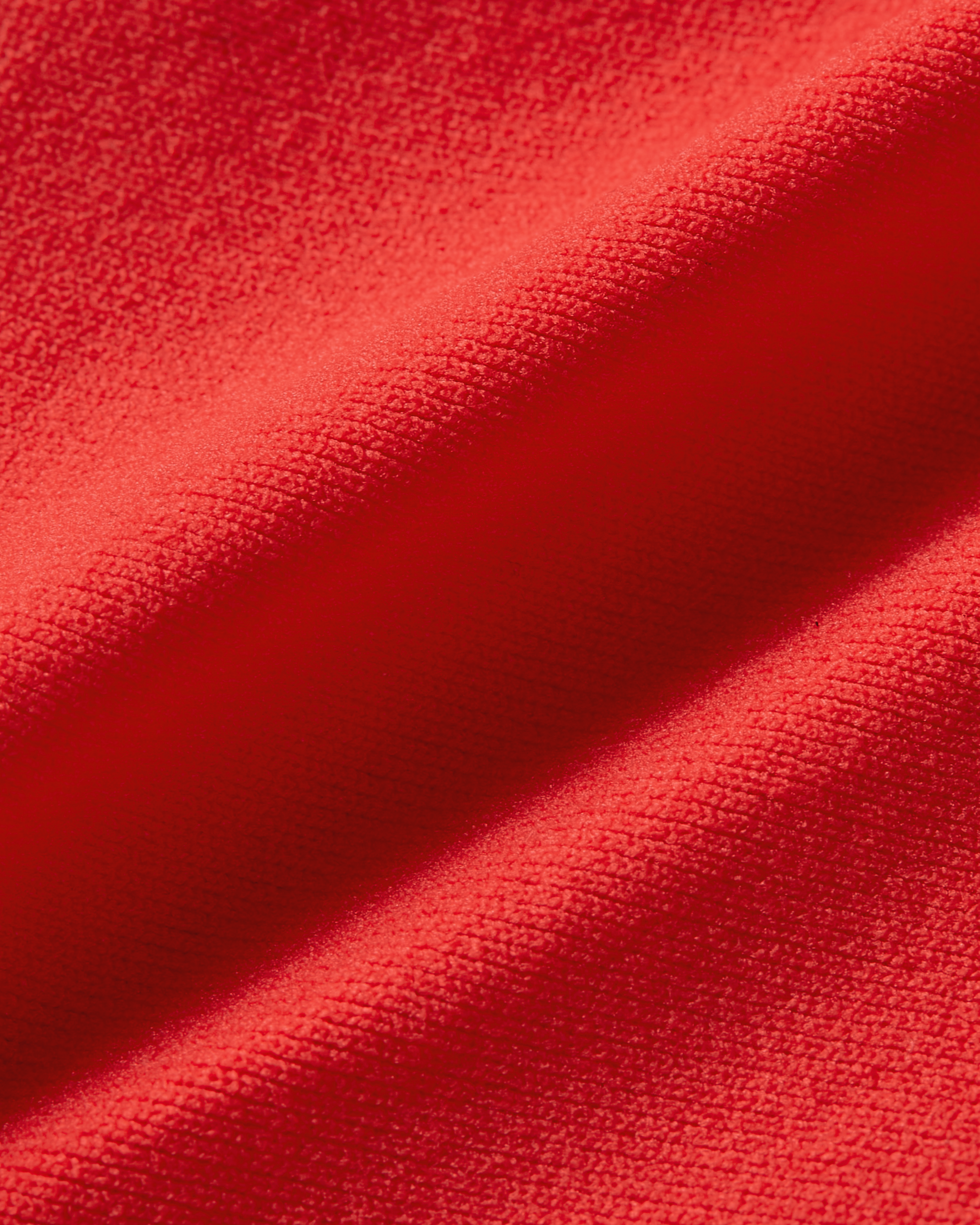 Fabric close-up of red Essentials thong, showcasing the vibrant color, smooth surface and supple, flexible structure of the material